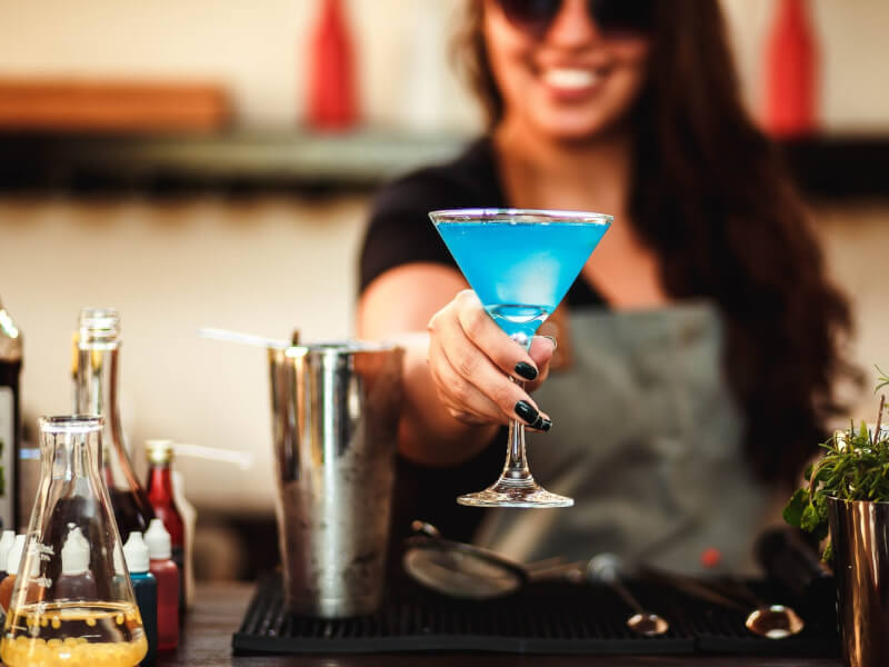 A person at a bar holding a blue cocktail